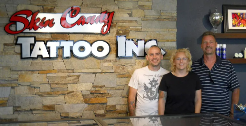 Skin Candy owners standing in front of the studio’s stone logo wall