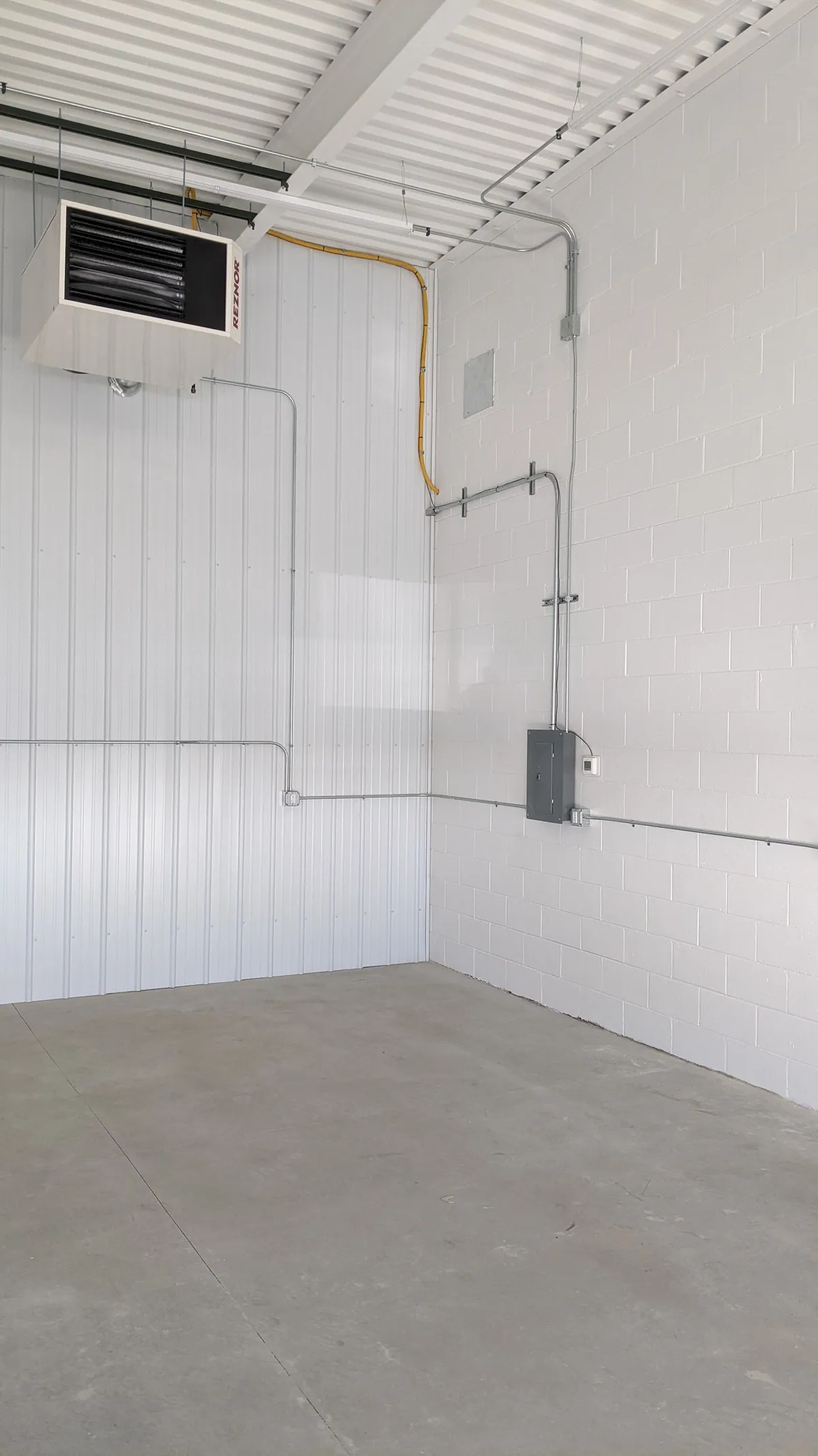 Empty white-walled buildout space with heater and electrical conduit