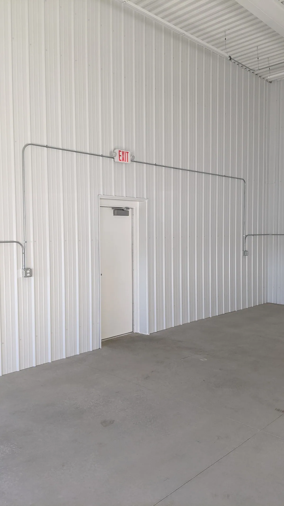 Buildout space with white metal walls and a single door